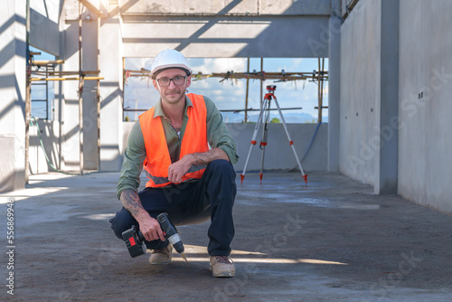 Male engineer wearing safety suit and hard hat holding toolbox and electric drill in construction site for building site survey in civil engineering project.