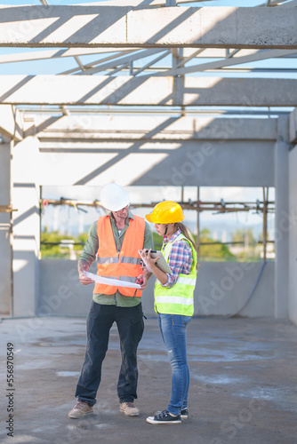 Two professionals inspect construction site of commercial building, industrial building, real estate project civil engineer, investor using laplet in background crane, skyscraper, concrete formwork