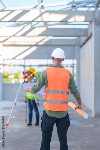 Construction Worker Using Theodolite Surveying Optical Instrument for Measuring Angles in Horizontal and Vertical Planes on Construction Site. Engineer and Architect Using blueprint Next to Surveyor. © ND STOCK