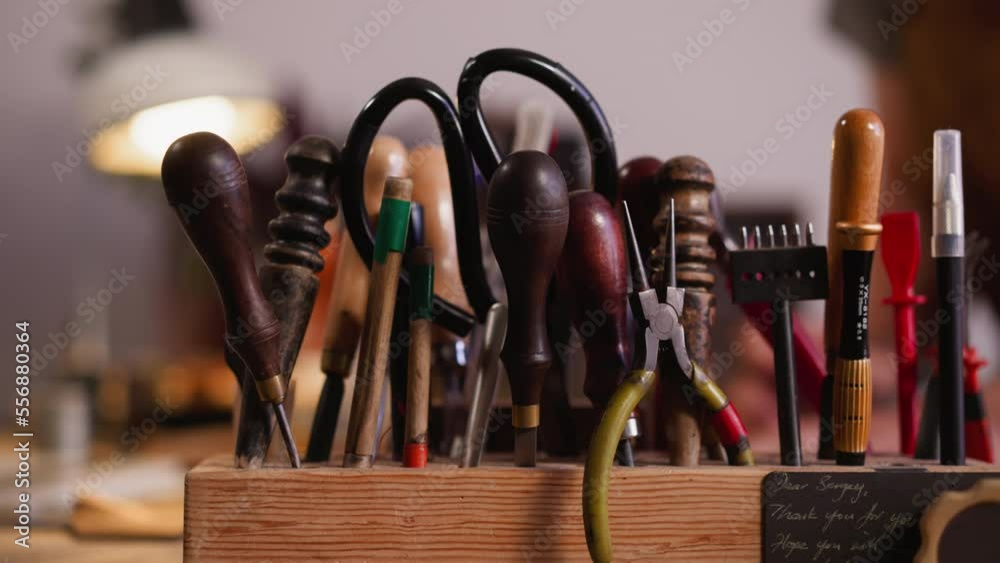 Wooden rack with kit of different leathersmith tools on workbench closeup. Instruments of professional craftsman in workshop. Manual work supplies