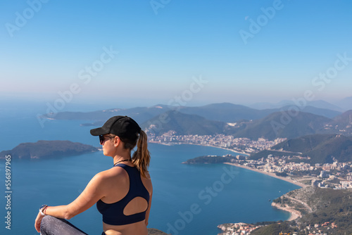 Hiking woman sitting on rock enjoying panoramic aerial view on coastline of Budva and Sveti Nikola Island seen from Goli Vrh, Adriatic Mediterranean Sea, Montenegro, Balkan, Europe. Budvanian Riviera
