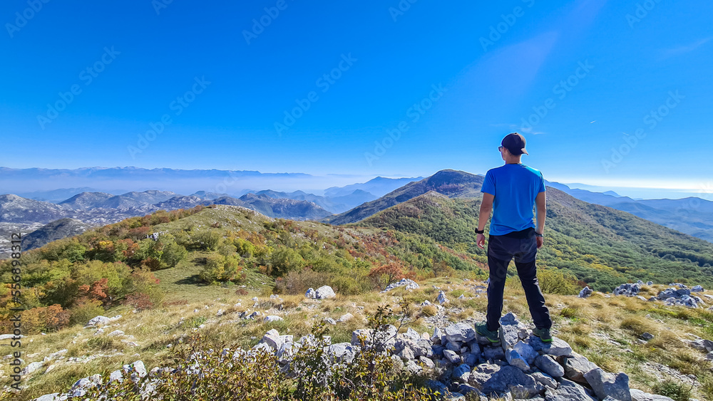 Man with backpack and hat on top of Goli Vrh with scenic view on mountain chains of Dinaric Alps and Lake Skadar National Park, Montenegro, Balkan, Europe. Valley covered by mystical fog. Freedom
