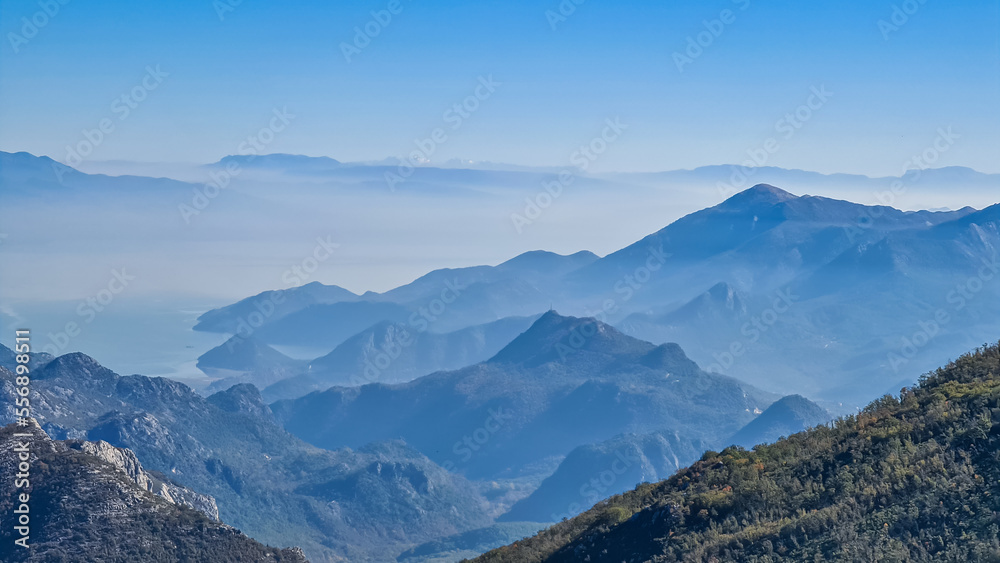 Panoramic view of dramatic karst mountain chains Dinaric Alps surrounding the Lake Skadar National Park seen from Goli Vrh, Montenegro, Balkan, Europe. Valley is covered by mystical fog, blue hills
