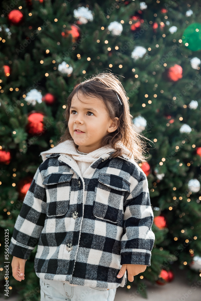 Adorable toddler girl standing next to Christmas tree outdoor, season holiday and childhood concept Adorable toddler girl standing next to Christmas tree outdoor, season holiday and childhood concept