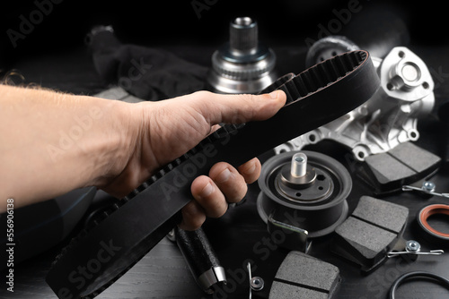 Timing belt and tension rollers of gas distribution system of car engine, concept of car maintenance. Master's hand holds timing belt against background of spare parts.