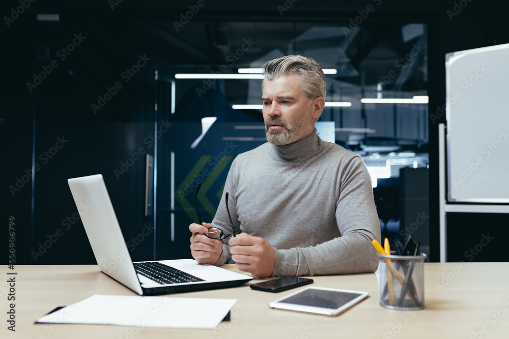 Serious thinking businessman inside office at work with laptop, senior gray haired man working sitting at desk. Serious thinking businessman inside office at work with laptop, senior gray haired man working sitting at desk.