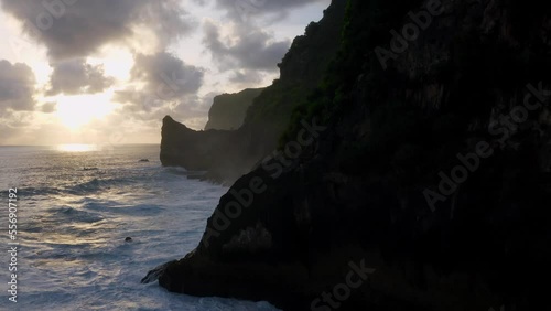 Silhouette of cliffs revealing the sunrise reflecting on ocean waves. Aerial, Nusa Penida Guyangan Falls, Bali, Indonesia photo