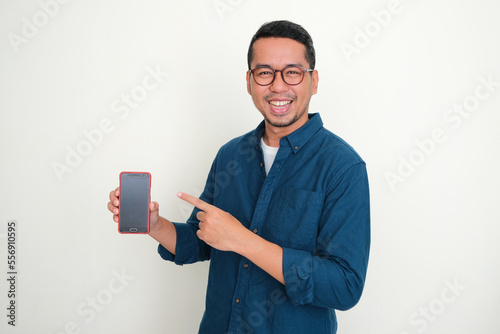 Adult Asian man smiling at the camera while pointing to blank phone screen that he hold photo