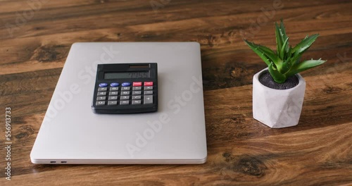 Businessman analysing provided information puts calculator with solved math equation on closed grey laptop by pot-flower. Freelancer finishes hard work day photo