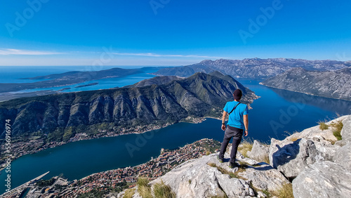 Man with panoramic view from Pestingrad (Derinski Vrh) of Kotor bay in sunny summer, Adriatic Mediterranean Sea, Montenegro, Balkan, Europe. Fjord winding along coastal towns. Lovcen, Orjen mountains