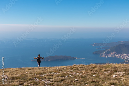 Hiking woman with backpack ascending to mountain summit of Goli Vrh. Panoramic aerial view on coastline of Budva and Sveti Nikola Island, Adriatic Mediterranean Sea, Montenegro, Balkan, Europe
