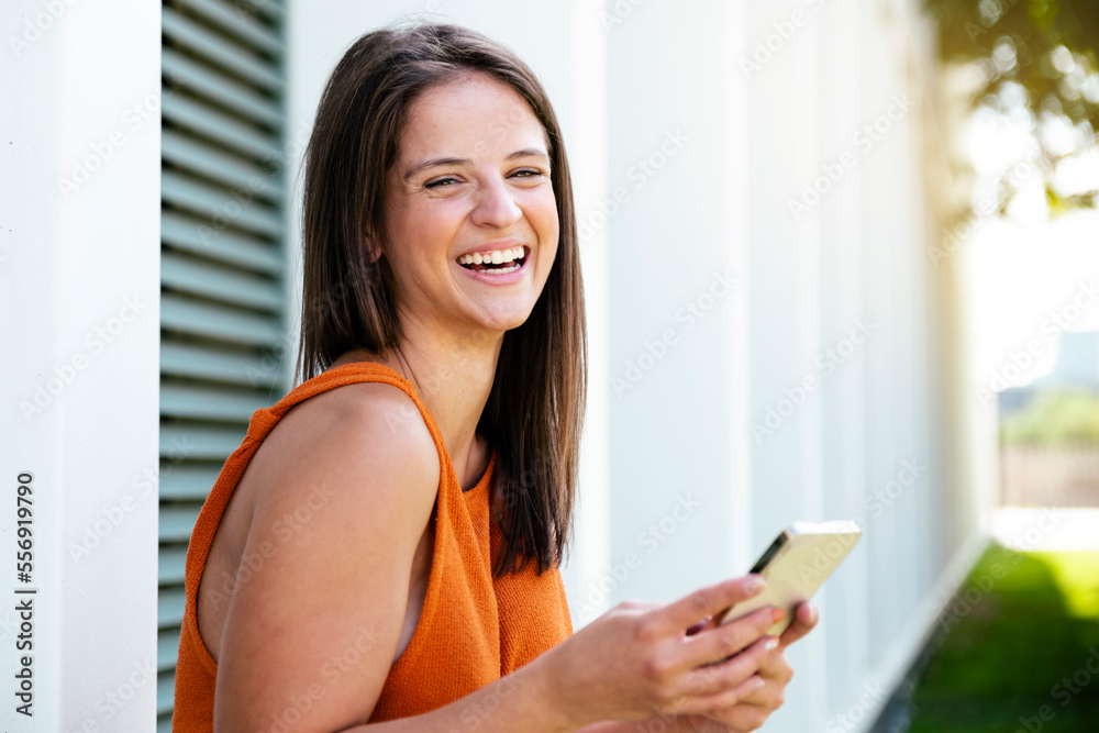 Cheerful woman looking at camera and smiling with a phone in the city - Hapiness, positive and lifestyle concept. Cheerful woman looking at camera and smiling with a phone in the city - Hapiness, positive and lifestyle concept.