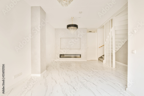 an empty living room with marble flooring and white walls there is a chandel light hanging from the ceiling photo