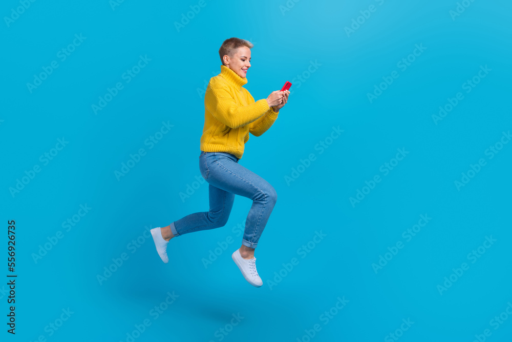 Full length photo of jump excited active influencer businesswoman wear yellow knitted jumper hold phone catch wifi isolated on blue color background