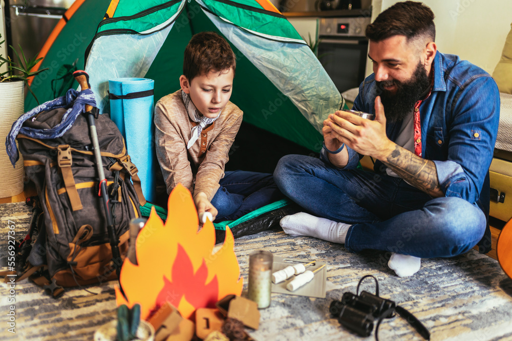 Dad with his son camp inside their home. They have pitched a tent and have a fake campfire. Dad with his son camp inside their home. They have pitched a tent and have a fake campfire.