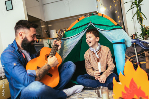 Dad with his son camp inside their home. They have pitched a tent and have a fake campfire. photo