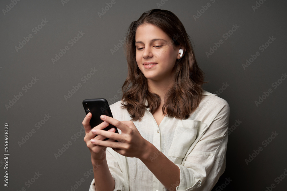 Lovely casual teen girl in earbuds and smartphone in hands, on dark background Lovely casual teen girl in earbuds and smartphone in hands, on dark background