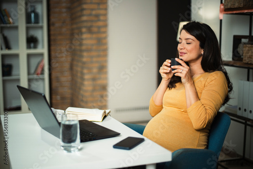 Pregnant woman in office. Beautiful businesswoman enjoy in fresh coffee.