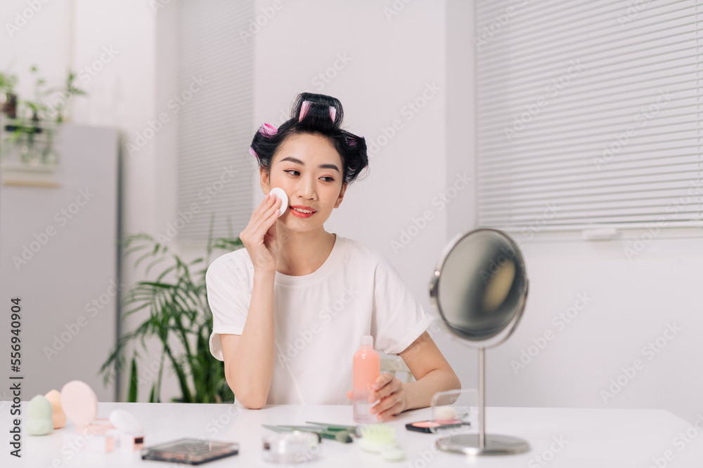 Young happy woman removing makeup from her face enjoying her skin and smiling at the mirror Young happy woman removing makeup from her face enjoying her skin and smiling at the mirror