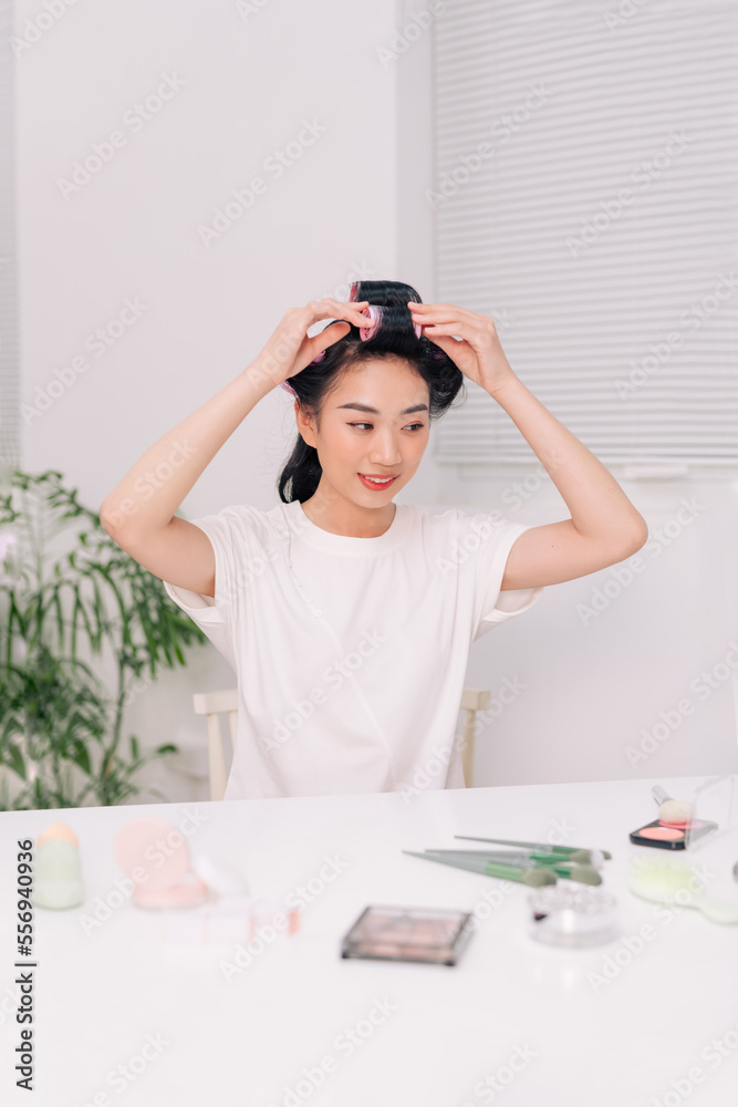 Close up portrait of Young beautiful girl having hair curlers on her head isolated on livingroom background Close up portrait of Young beautiful girl having hair curlers on her head isolated on livingroom background