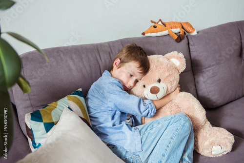 Εκτύπωση καμβά Sad little boy holding teddy bear and sitting on sofa at living room