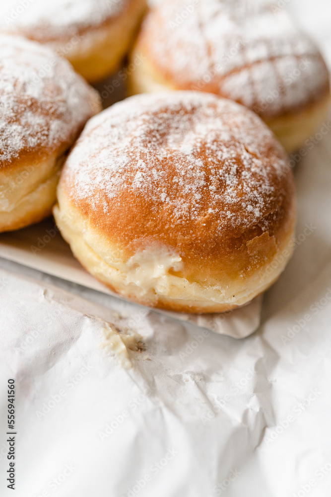 Krapfen, Berliner doughnuts or Pfannkuchen with powdered sugar filled with custard wrapped in white paper fresh from German bakery, traditional fried yeast dough pastry for New Year or carnival party Krapfen, Berliner doughnuts or Pfannkuchen with powdered sugar filled with custard wrapped in white paper fresh from German bakery, traditional fried yeast dough pastry for New Year or carnival party