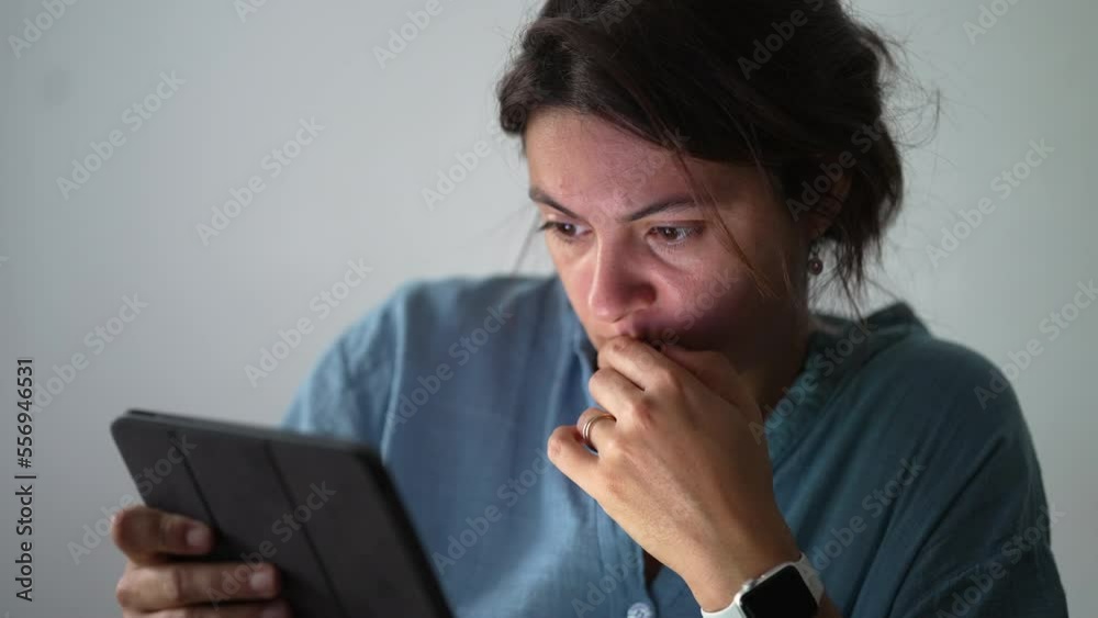 Anxious Woman staring at tablet with concerned emotion. Preoccupied expression of female person looking at screen browsing internet using technology Anxious Woman staring at tablet with concerned emotion. Preoccupied expression of female person looking at screen browsing internet using technology