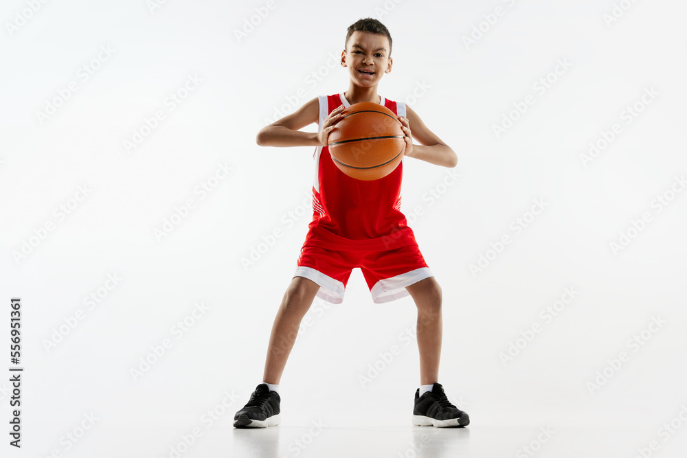 Portrait of boy in red uniform training, playing basketball over grey studio background. Sportive spirit Portrait of boy in red uniform training, playing basketball over grey studio background. Sportive spirit