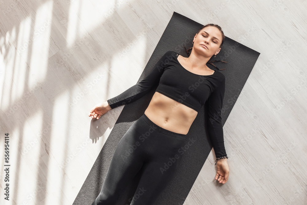 Woman practicing yoga, doing shavasana exercise, relaxation pose, lying on mat in sportswear in room, top view
