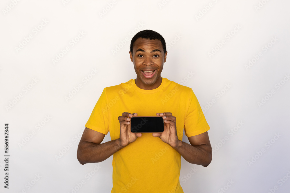 Portrait of cheerful young man showing mobile phone over white background. African American guy wearing yellow T-shirt advertising cellphone. Promotion concept Portrait of cheerful young man showing mobile phone over white background. African American guy wearing yellow T-shirt advertising cellphone. Promotion concept