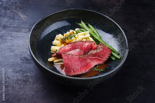 Traditional Italian chianina sliced roast beef with gnocchetti sardi pasta and beans in spicy red wine sauce served as close-up in a Nordic design bowl with copy space