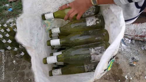 Hard-working Asian young lady earns by collecting green wine bottles and then packing them in sacks to be sold to liquor bottlers. photo