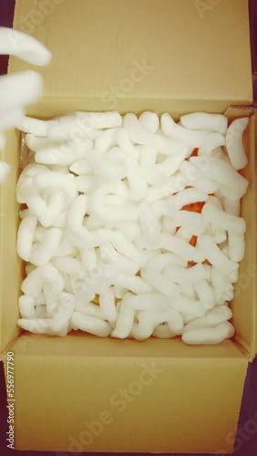 Vertical video social media format – Closeup overhead shot of items in a cardboard box, with loosefill polystyrene protective packing, being poured over the top, ready for shipping / posting. photo