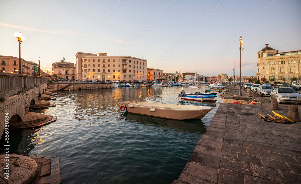 Fishing boats on the water in Ortigia island with the cityscape of Syracuse in the evening