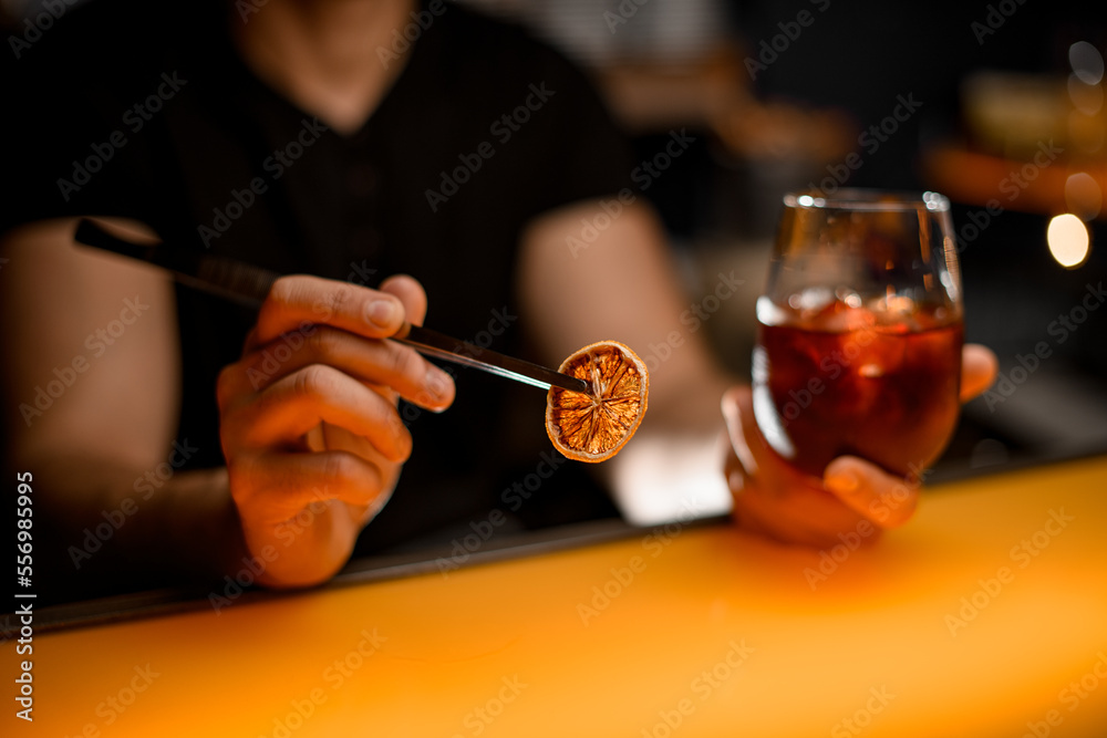 selective focus on male bartender hand holding tweezers with dry orange slice
