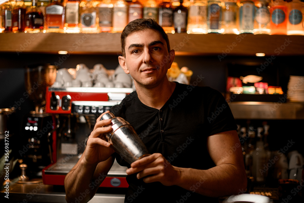 Male barman in bar shaking and mixing alcohol cocktail with shaker in hands.