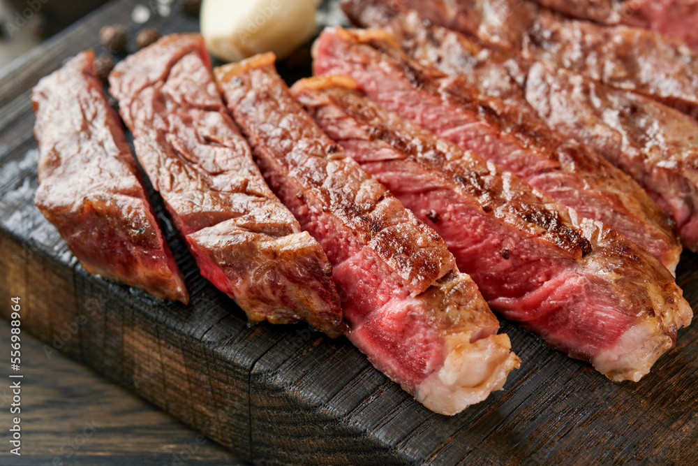 Steaks. Sliced grilled meat steak New York or Ribeye with spices rosemary and pepper on black marble board on old wooden background. Top view. Mock up. Steaks. Sliced grilled meat steak New York or Ribeye with spices rosemary and pepper on black marble board on old wooden background. Top view. Mock up.