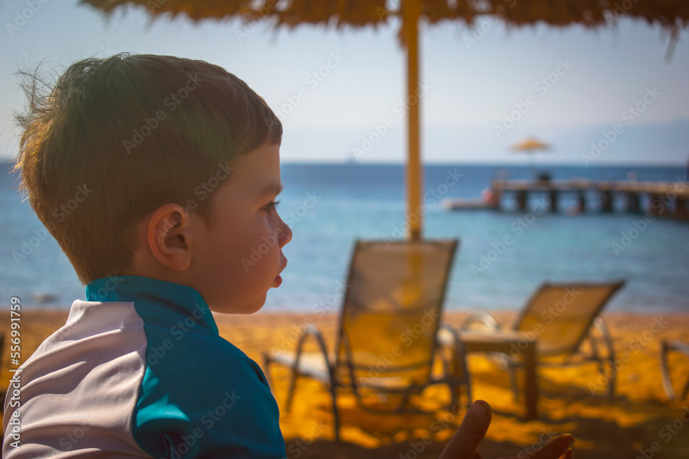 Fototapeta premium Cool Young Boy playing on the beach dressed in a rash guard suit, travel tourism concept on an exotic beach 