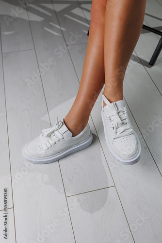 Perfect female legs in white classic sneakers. Beautiful female legs in summer shoes in white shoes.