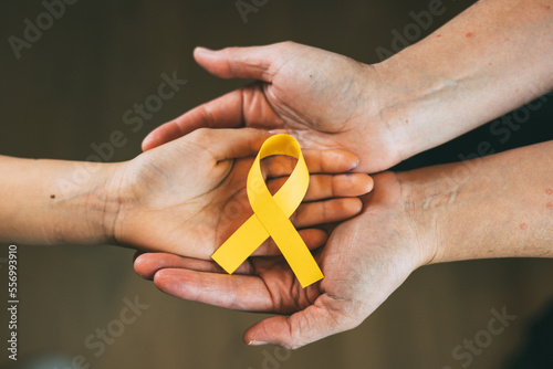 Woman's hands holding child hand with a yellow ribbon, world cancer day concept