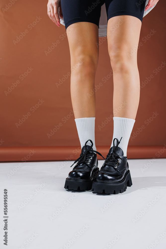 Beautiful female legs in leather black lace-up oxford shoes. Female legs with fashionable shoes and white socks. Casual black women's shoes Beautiful female legs in leather black lace-up oxford shoes. Female legs with fashionable shoes and white socks. Casual black women's shoes