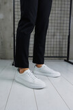 Close-up of male legs in black pants and white casual classic sneakers. Men's summer leather shoes