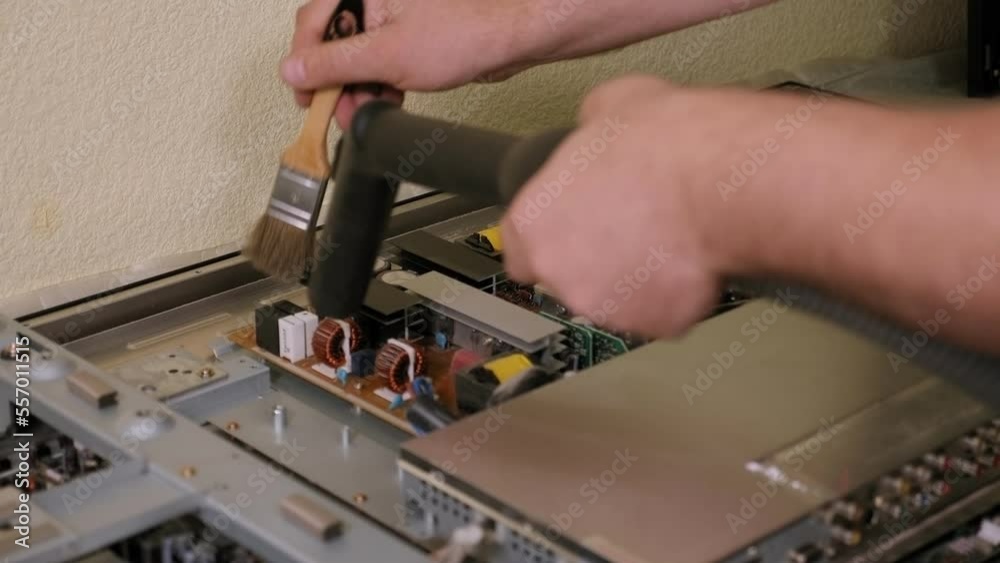 Close-up of a technician vacuuming a TV during repairs in the workshop. The TV is clean in the service center. Close-up of a technician vacuuming a TV during repairs in the workshop. The TV is clean in the service center.