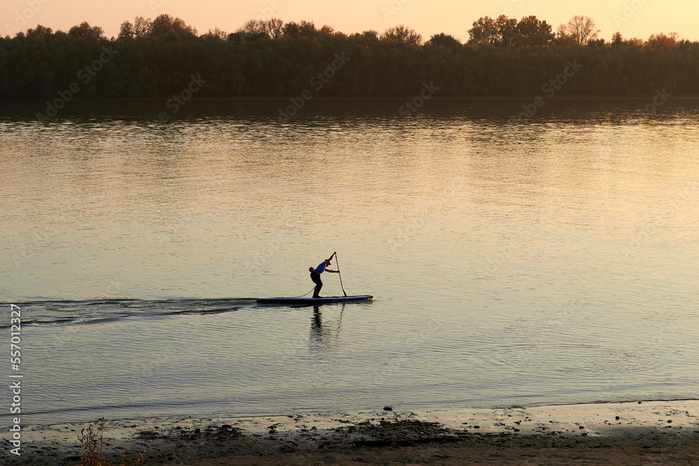 Sporty man rowing on stand up paddle (SUP) at calm Danube river at autumn
