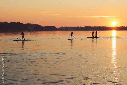 Silhouettes of paddlers on stand up paddle board (SUP) at sunrise on quiet surface of river