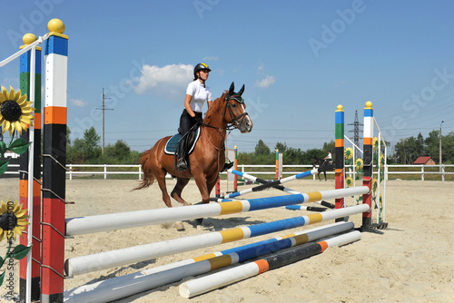 Young female jockey on horse jumps over a barrier on training.