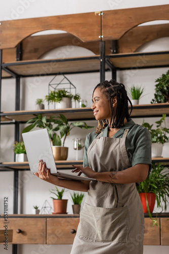 Cuadro en lienzo happy african american florist in apron holding laptop and looking away in flowe