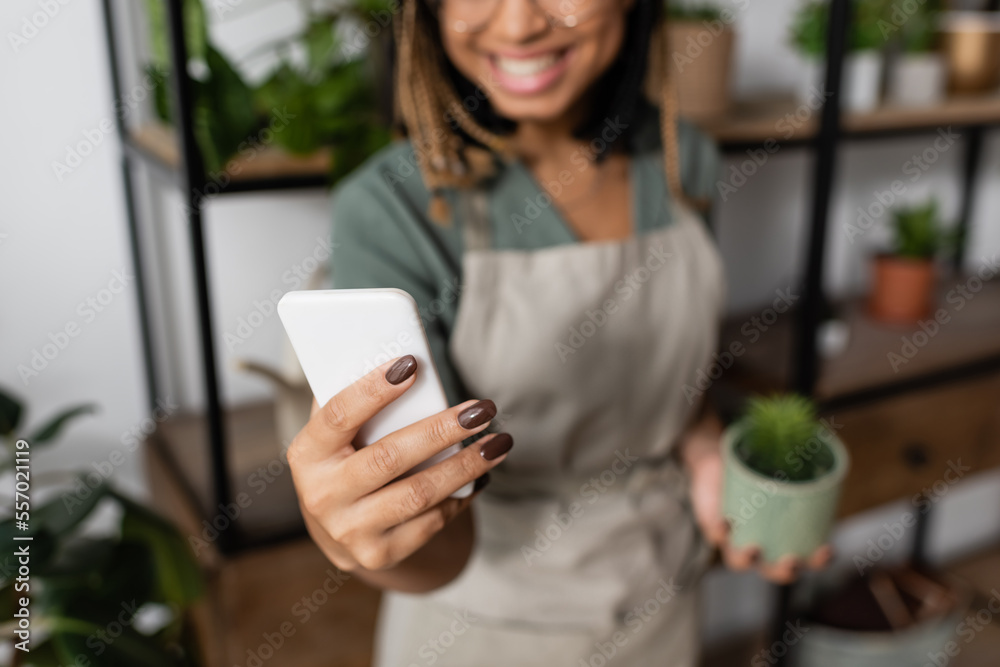 partial view of smiling african american woman holding smartphone during video call in flower shop partial view of smiling african american woman holding smartphone during video call in flower shop