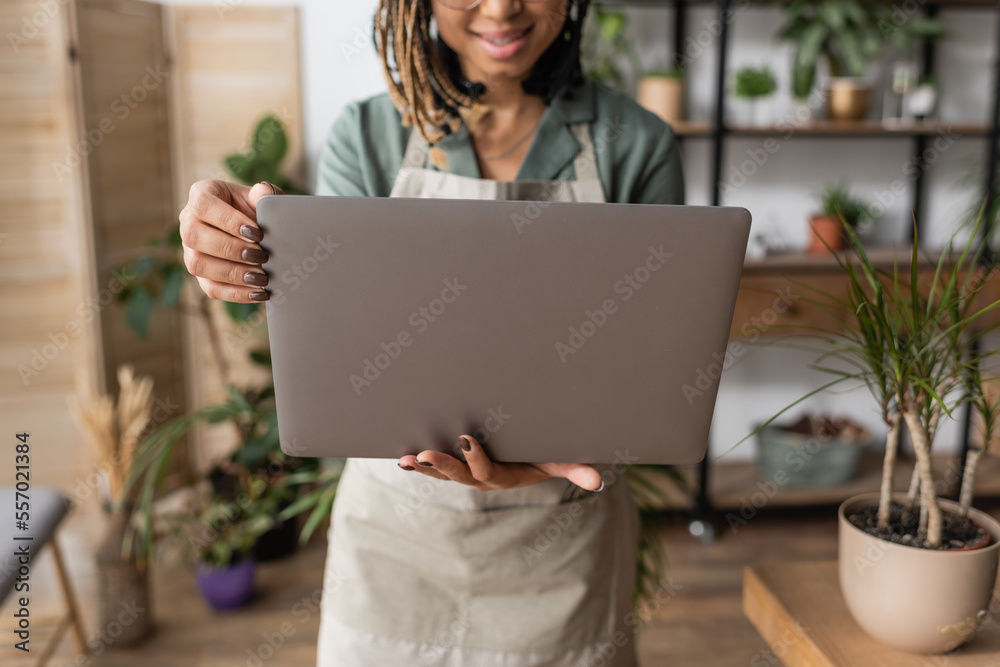 partial view of blurred african american florist standing with laptop in flower shop partial view of blurred african american florist standing with laptop in flower shop
