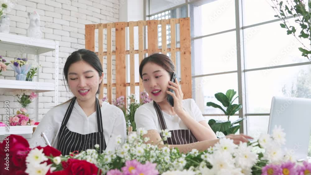 Asian florist Females talking on mobile phone with clients or customers at flower shop together, Woman receiving order of flowers, taking note on notebook, working on laptop, Small business, Entrepren Asian florist Females talking on mobile phone with clients or customers at flower shop together, Woman receiving order of flowers, taking note on notebook, working on laptop, Small business, Entrepren